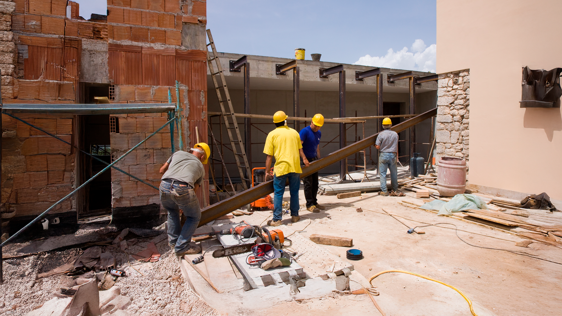 Imagen ilustrativa. Trabajadores de la construcción mueven materiales en área de construcción de vivienda.